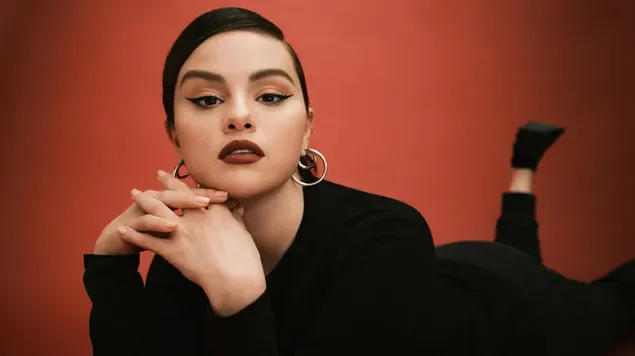 歌手で女優のセレーナ・ゴメスは、背景が赤のすべて黒の衣装を着ています。