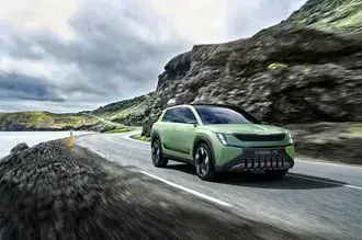 Tapeta Škoda Vision 7S se zelenými ocelovými ráfky jízda u moře na asfaltové silnici mezi horami za oblačného počasí 2K