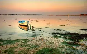 Small wooden boat on the water at sunset 2K wallpaper