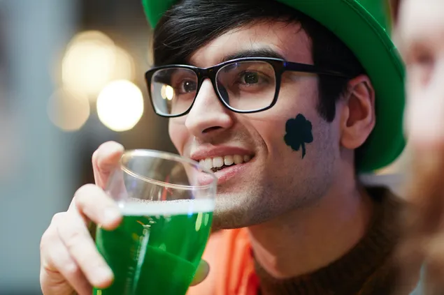 Pria yang tersenyum dengan tato semanggi meminum minuman hari Saint patrick hijau
