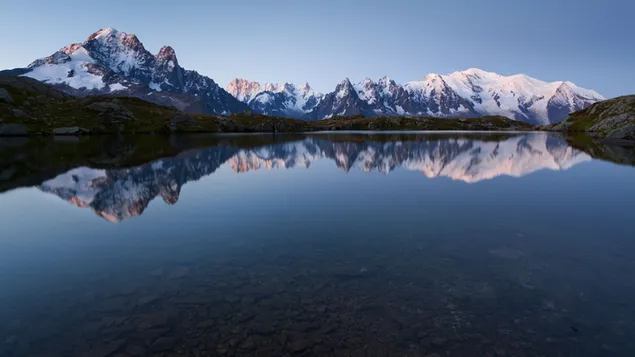Picos de montaña nevados y reflejo del cielo despejado en agua clara 4K fondo de pantalla