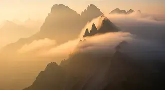 soft morning light filters through dense mist, gently revealing the silhouettes of rugged mountain peaks in a serene and ethereal landscape