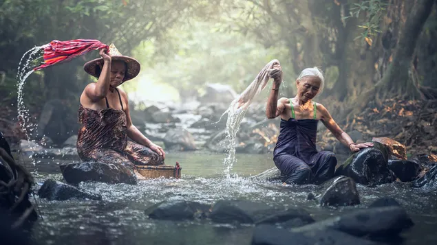 Sombreros de paja asiáticos y ancianas lavando ropa en el arroyo