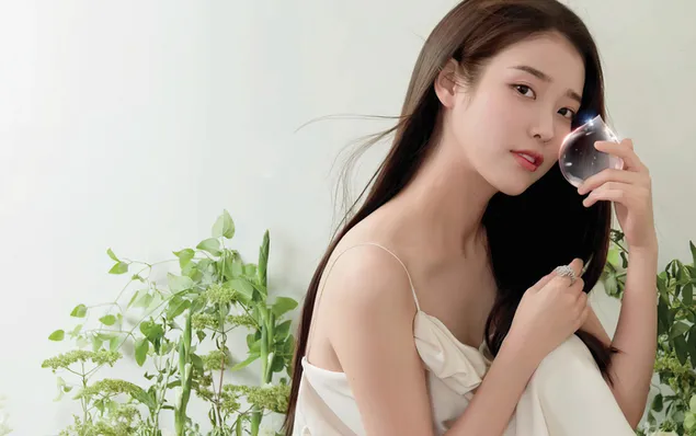 South Korean beautiful female singer IU poses in front of a white background with a glass of green plants