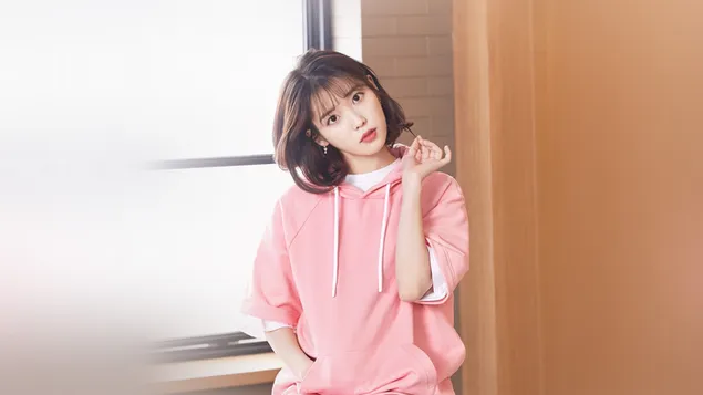 South Korean beautiful singer IU with short brown hair in a pink dress at home by the window