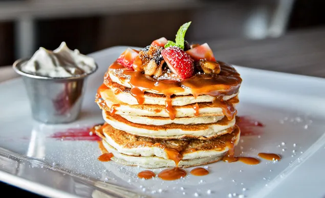 Stack of pancakes top with fruits and Maple syrup in a plate