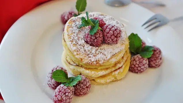 Stack of pancakes with frosted raspberry sprinkled with powdered sugar for breakfast