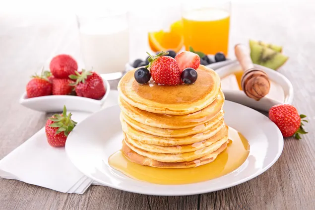 Stack of pancakes with honey and berries on top and a glass of orange juice  download