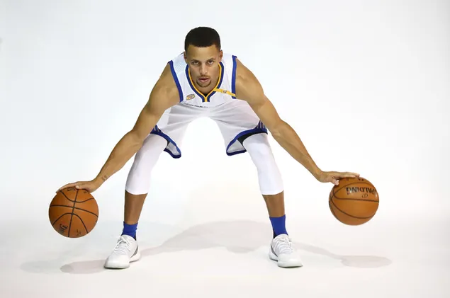 Stephen Curry berpose dengan jersey tim biru, kuning dan putih dan sepatu kets putih sambil memegang dua bola basket.