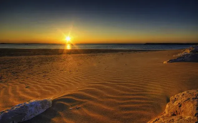 La luz del sol que se eleva más allá del mar golpea las arenas de la playa 2K fondo de pantalla