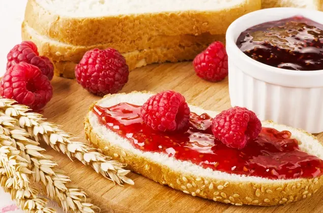 スライスされたパンは、ラズベリージャムとラズベリーフルーツとジャムの小さなボウルで広げられます