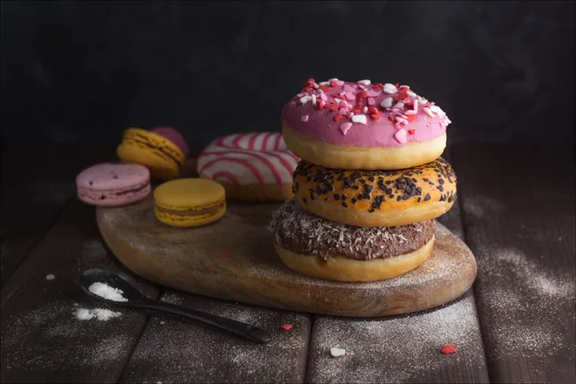 saldzios bandeles ir geltonai roziniai macarons su cukraus pudra ant medines lekstes patiekiami juodu saukstu ant medinio stalo. atsisiusti