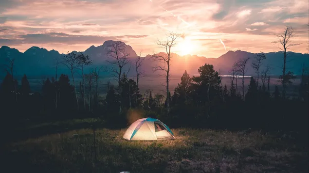 Tenda berkemah dengan penerangan di tengah pegunungan dan pepohonan saat matahari terbenam