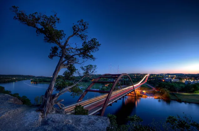 Gecenin mavi tonlarında şehir ışıkları ve köprüden geçen arabaların uzun pozlama görüntüsü 2K duvar kağıdı