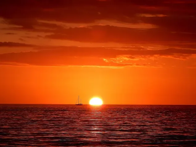 The setting sun and the silhouette of the ship in the red sky beyond the sea download
