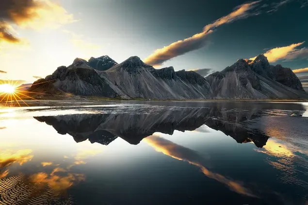 The sun rising through the dark clouds behind the mountains reflected in the lake water