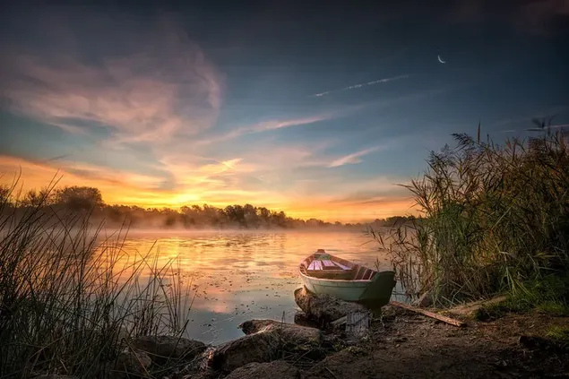 Winziges Boot am Seeufer mit gelber Wolkenansicht bei Sonnenuntergang herunterladen