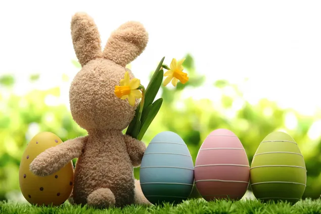 Spielzeughase, der Ostern mit Blumen in der Nähe von vier farbigen Eiern feiert 2K Hintergrundbild