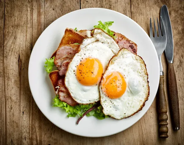 Two sunny side up eggs with ham and lettuce in a round white plate ready for breakfast