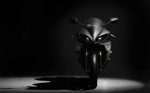 Una imponente motocicleta Yamaha negra descansando en el suelo iluminada por una luz blanca sobre un fondo negro