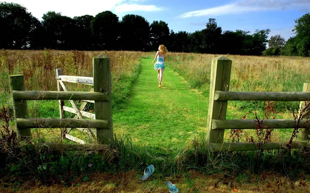 pamje e gruas se bukur bjonde qe vrapon e lumtur mes pemeve dhe bimeve jashte pas gardhit prej druri shkarkim