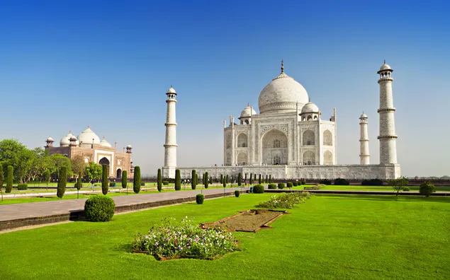 pohled na taj mahal, jedinecne architektonicke dilo v bile barve, s nadhernymi zelenymi rostlinami a jasnou oblohou stahnout