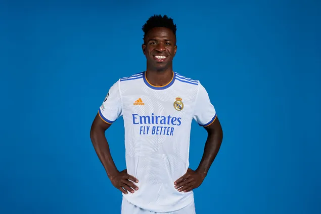 Vinicius Junior poses with her hands on her hips in front of a blue background 2K wallpaper