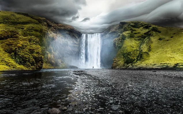 Wasserfall, der durch Wolken zwischen grünen Klippen fließt 2K Hintergrundbild