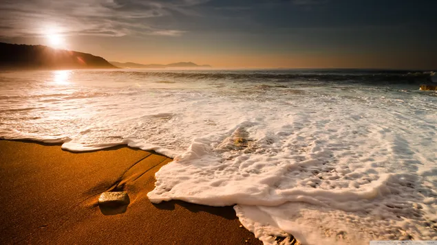 朝の太陽の最初の光線が海に反射する、ビーチの毛布に似た波