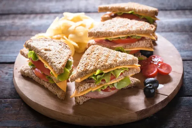 Sandwich clubhouse roti gandum dengan tomat, zaitun, dan keju di papan kayu