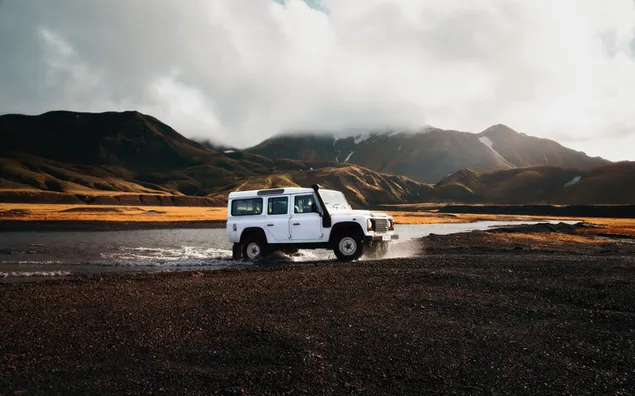 Jeep de coche blanco remolcado en un camino de tierra junto al río en un día nublado y nublado