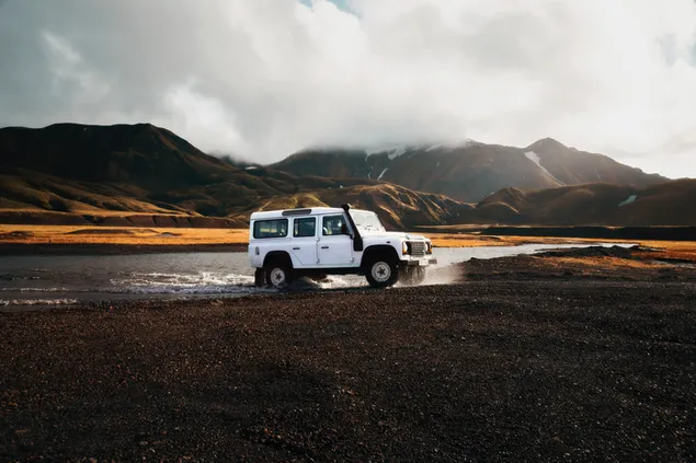 Land Rover blanco 4X4 en un río con fondo de montañas