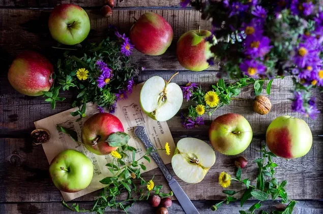 Apel utuh dan irisan dengan bunga kuning dan ungu di meja kayu