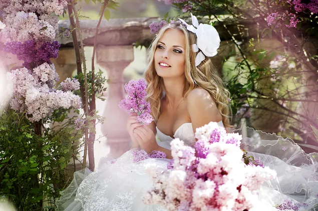 Frau in wunderschönem Hochzeitskleid zwischen lila Blumen mit weißem Rosenaccessoire im Haar