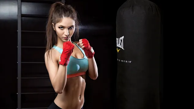 Woman in green sports suit and red gloves boxing on a punching bag and hair tied. 2K wallpaper