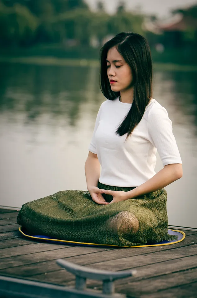 mujer meditando en un muelle de madera durante el día