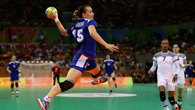 Women playing handball with their white and blue jerseys in the crowded stadium 2K wallpaper
