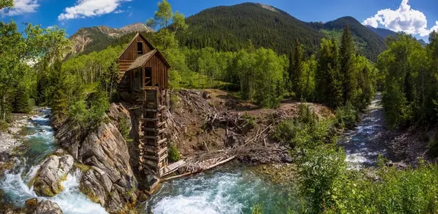 Pemandangan indah pegunungan, pohon, dan rumah kayu di sekitar sungai dalam cuaca mendung