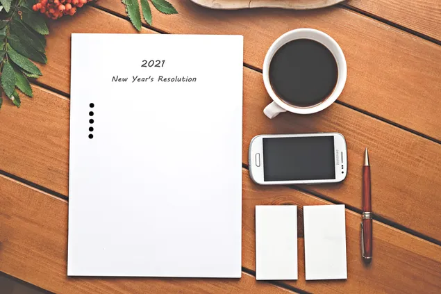 Written 2021 New Year's resolution with mobile and coffee 