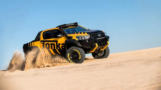 Gele en zwarte Ford pick-up op wielen met grote opdruk die buiten op woestijnzand rijdt