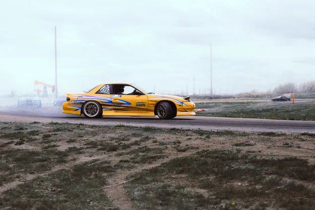 Gele en blauwe coupé drijft overdag op zwarte asfaltweg