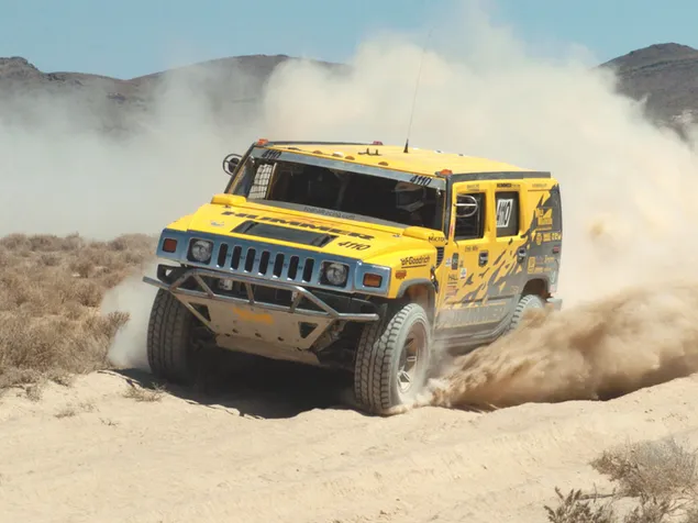 Yellow Hummer driving in dust on a dirt road between mountains 2K wallpaper
