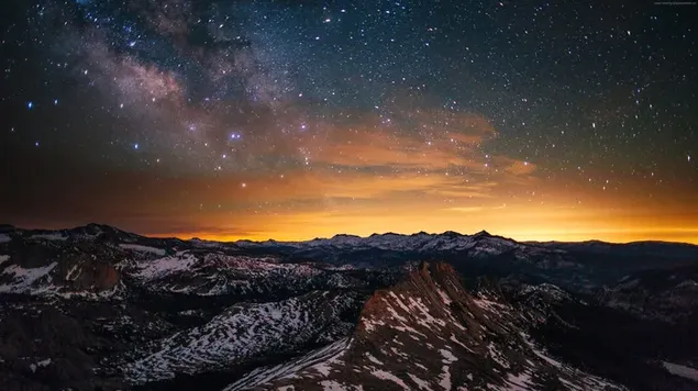 Yellow lights on the horizon and snowy mountain peaks in the night starry sky