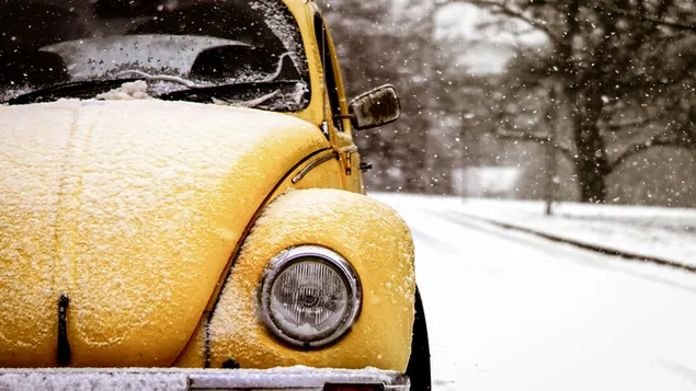 Gele volkswagen kever op weg bedekt met sneeuw