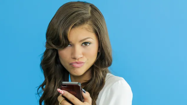 Zendaya posing cute with her phone in hand in white outfit with black long hair
